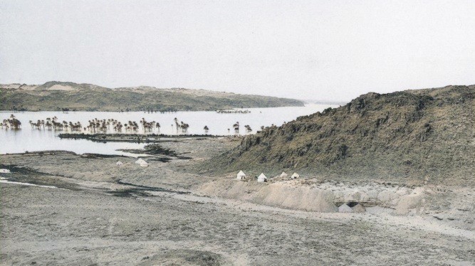Cemetery 17 at Khor Bahan on the higher terrace of the khor, to the right of the white tents. The alluvial plain was already flooded behind the Aswan Dam as the palm trees would have lined the riverbank. Photo from Reisner (1910: plate 23/b). Colorized by cutout.pro.